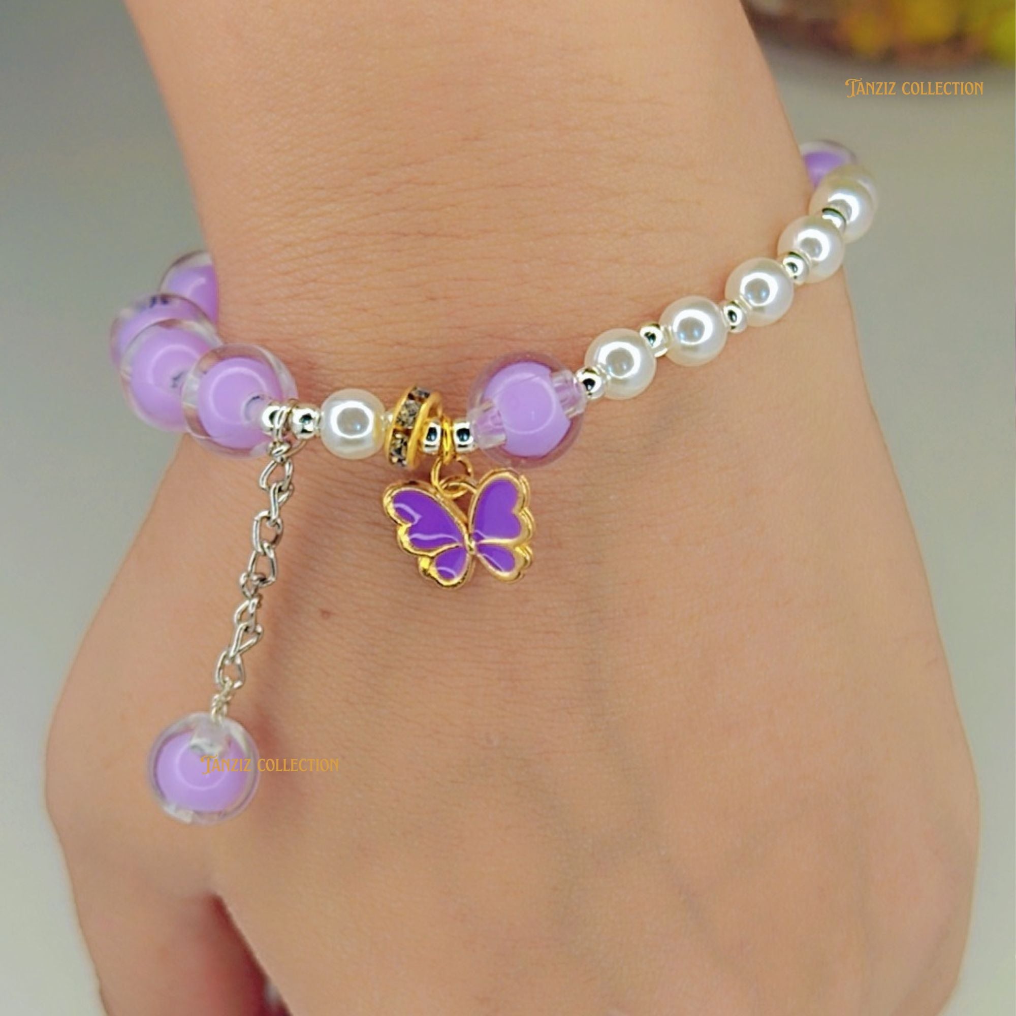 Beaded bracelet with a purple butterfly charm on a wrist against a neutral background