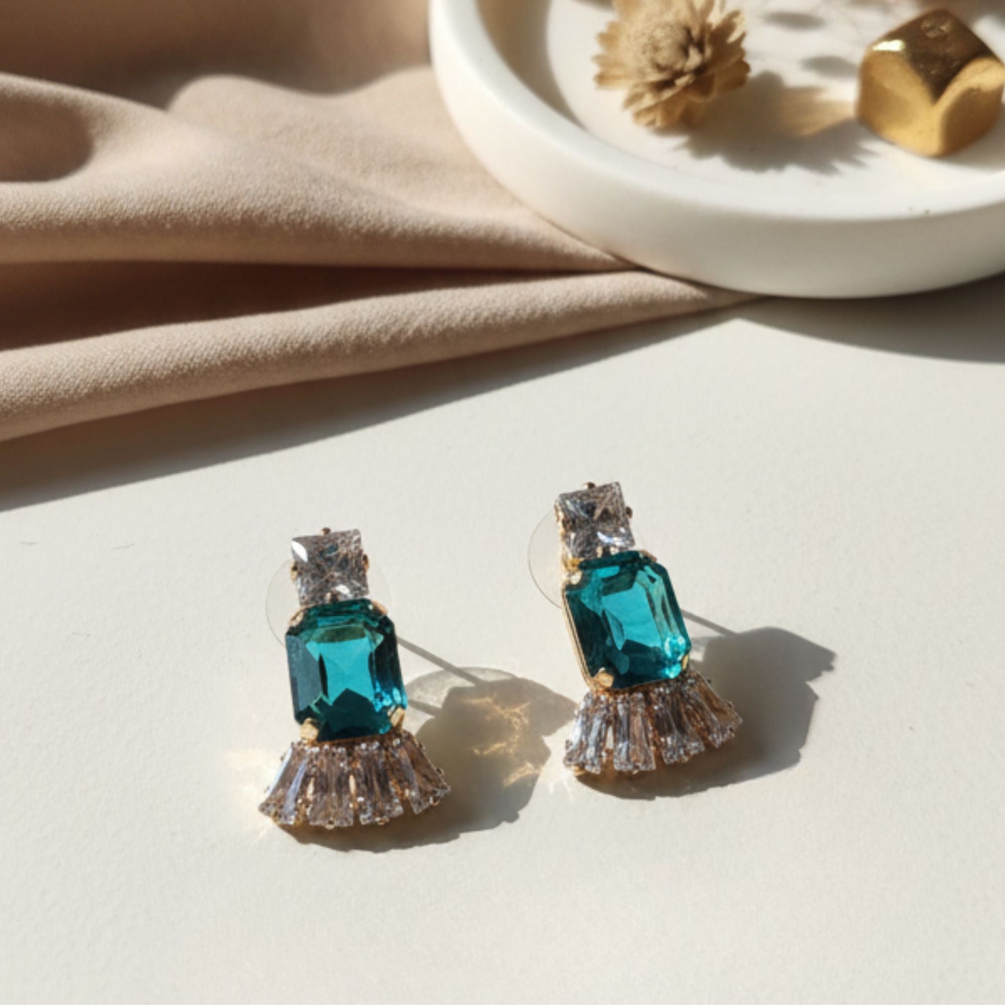 Teal emerald-cut crystal earrings with square and baguette stones on beige tabletop with ceramic dish – luxury fashion jewelry